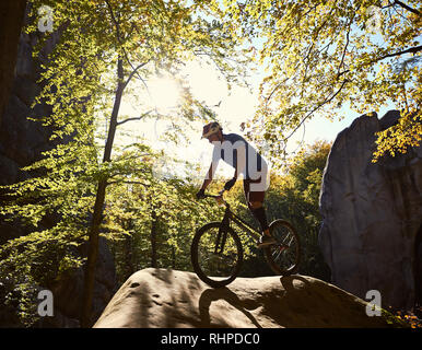 Junge männliche Radfahrer Balancieren auf Trial Fahrrad, akrobatische Tricks auf Big Boulder im Wald im Sommer sonnigen Tag. Konzept der Extreme Sport aktiven Lebensstil Stockfoto