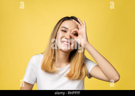 Asiatische junge Frau mit ok Zeichen Geste isolieren auf gelben Hintergrund. Stockfoto