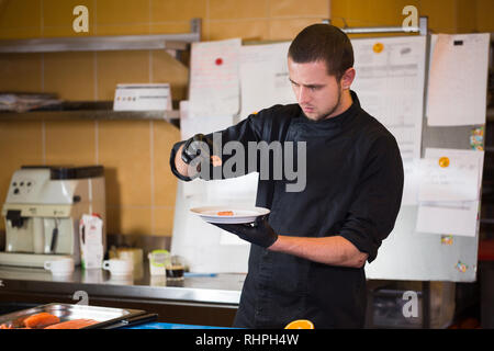 Thema kochen ist Beruf des Kochens. Portrait der kaukasischen Mann im Restaurant Küche vorbereiten rot Fischfilets Lachs Fleisch in schwarz Handschuhe einheitliche Stockfoto