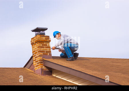 Auftragnehmer Builder mit blauen hardhat auf dem Dach abdichten Kamin Stockfoto
