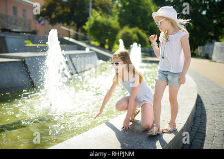 Zwei süße kleine Mädchen, die durch die Stadt Brunnen an einem warmen und sonnigen Sommertag. Kinder Spaß mit Wasser im Sommer. Aktive Freizeitgestaltung für Kinder. Stockfoto