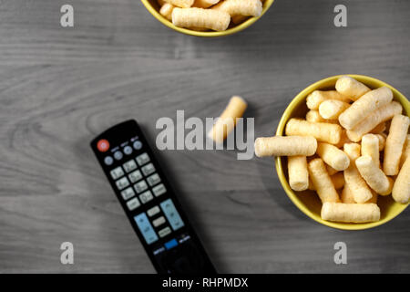 Mais Puffs auf Schalen über Tisch in der Nähe der TV-Fernbedienung. TV Steuerung und Snacks, Filme Konzept Stockfoto