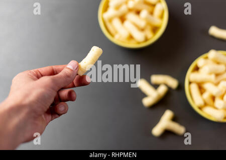 Hand corn Puffs (pufuleti) über den Tisch. Fokus auf Mais Puffs/Snacks Stockfoto