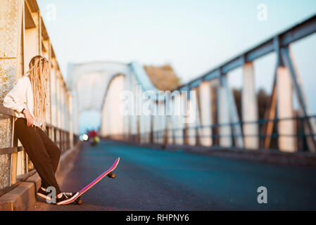 Junge Frau mit Skateboard auf Brücke Stockfoto