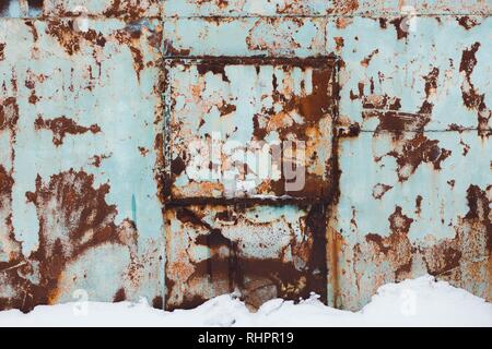 Das Metall Wand der blauen Schatten ist rostig mit Zeit- und Wetterbedingungen. Es ist Winter und es gibt eine Menge weißer Schnee auf dem Boden. Stockfoto
