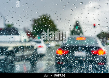Regentropfen auf der Windschutzscheibe an einem regnerischen Tag; Autos gestoppt an einer Ampel im Hintergrund; Kalifornien Stockfoto