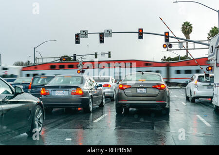 Februar 2, 2019 Sunnyvale/CA/USA - Fahrzeuge warten an einer roten Ampel; high speed Zug passiert im Hintergrund, San Francisco Bay Area, C Stockfoto