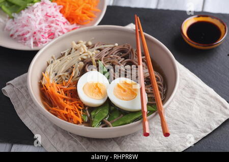 Japanisch Suppe mit enoki Pilze, Soba Nudeln, gekochte Eier, Karotten, Rettich, grüne Bohnen und Sojasauce Stockfoto