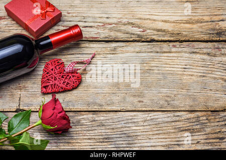 Valentines Tag Konzept. Flasche Wein, rote Rose, Geschenkbox, wicker Herz auf einem rustikalen hölzernen Tafel mit Kopie Platz für Text. Stockfoto