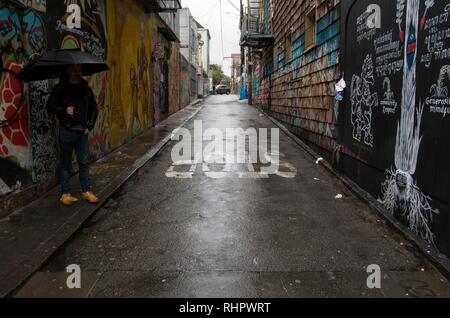 Ein Mann schützt sich vor Regen mit einem Regenschirm beim Stehen in Clarion Gasse in San Francisco, wo viele Stücke von Street Art. Stockfoto