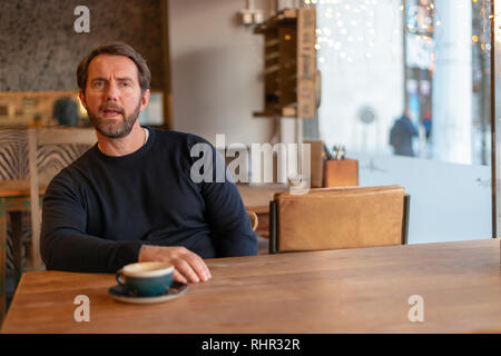 Im mittleren Alter kaukasischer Mann am Tisch im Café zum Ausdruck der Ungläubigkeit und Abneigung sitzen Stockfoto