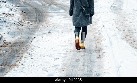 Winterspaziergang in Gelb Leder Stiefel. Zurück Blick auf die Füße der Frauen zu Fuß entlang der eisigen verschneiten Pflaster. Paar Schuh auf vereisten Straße im Winter. Abstra Stockfoto
