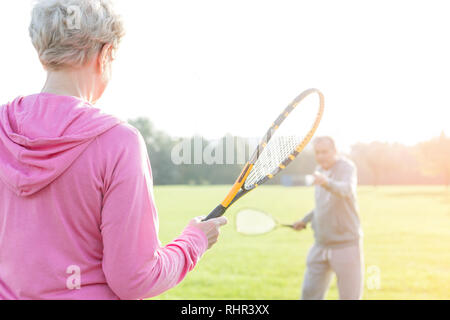 Ältere Frau mit Tennis bat beim Spielen mit Mann im Park Stockfoto
