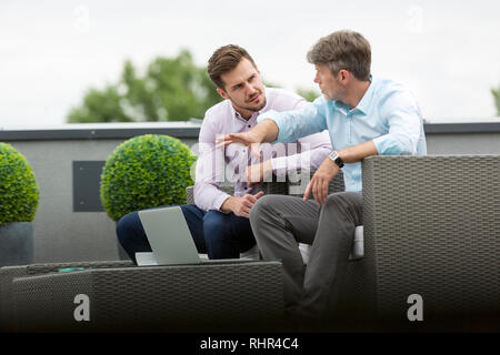 Unternehmer diskutieren über Laptop beim Sitzen im Büro Terrasse Stockfoto