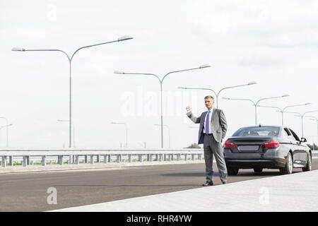 Reifen Geschäftsmann per Anhalter Fahren im Stehen mit aufschlüsselung Auto auf der Straße Stockfoto