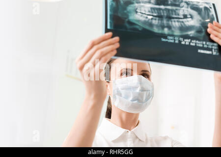 Weiblichen Zahnarzt maskierter während der Prüfung x-ray an zahnmedizinische Klinik Stockfoto