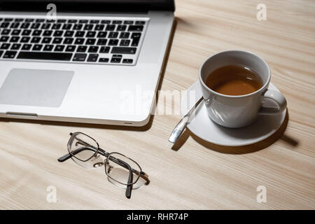 Schreibtisch mit Laptop, Brillen und einer Tasse Tee auf einem Holztisch - Bild Stockfoto