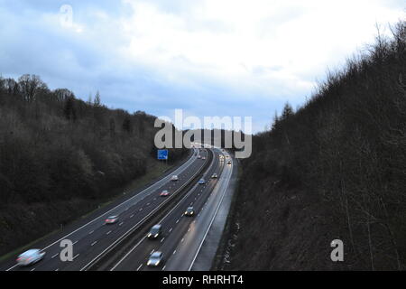 Datenverkehr läuft frei auf M25, zwischen der Anschlussstelle 4-5, wie es durch einen Schnitt in die North Downs in der Nähe von Shoreham, Kent bei Piloten Holz geht. Winter Dämmerung Stockfoto