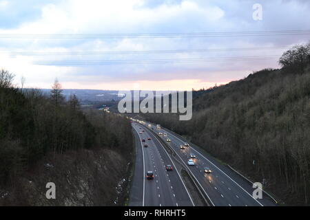 Datenverkehr läuft frei auf M25, zwischen der Anschlussstelle 4-5, wie es durch einen Schnitt in die North Downs in der Nähe von Shoreham, Kent bei Piloten Holz geht. Winter Dämmerung Stockfoto