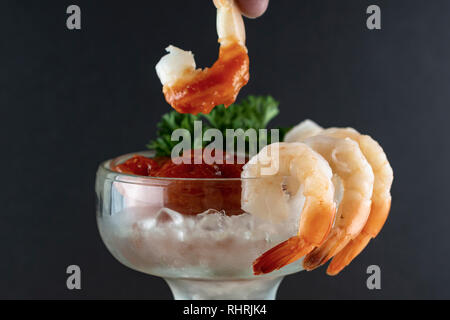 Tauchen eine Garnele in Cocktailsauce. Fingertip nur sichtbar. Krabbencocktail mit Garnelen auf der Seite des Glases hing. Schwarzen Hintergrund. Stockfoto