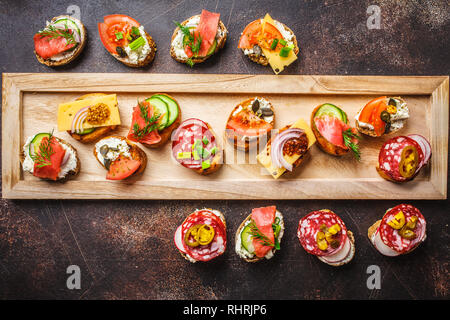 Verschiedene spanische Tapas mit Fisch, Wurst, Käse und Gemüse. Dunkler Hintergrund, flach. Stockfoto
