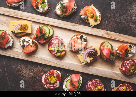Verschiedene spanische Tapas mit Fisch, Wurst, Käse und Gemüse. Dunkler Hintergrund, flach. Stockfoto