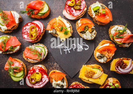Verschiedene spanische Tapas mit Fisch, Wurst, Käse und Gemüse. Dunkler Hintergrund, flach. Stockfoto