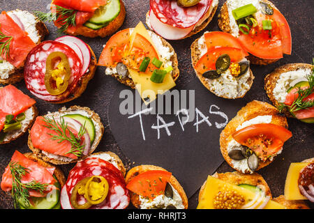 Verschiedene spanische Tapas mit Fisch, Wurst, Käse und Gemüse. Dunkler Hintergrund, flach. Stockfoto