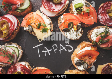 Verschiedene spanische Tapas mit Fisch, Wurst, Käse und Gemüse. Dunkler Hintergrund, flach. Stockfoto