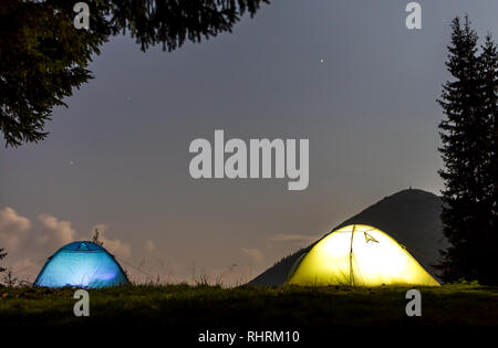 Zwei hell leuchtende, touristische Zelte auf der grünen Wiese Wald Lichtung auf dunklen Berg und dem klaren, blauen Sternenhimmel Kopie Raum Hintergrund. Tourismus, Nacht campin Stockfoto