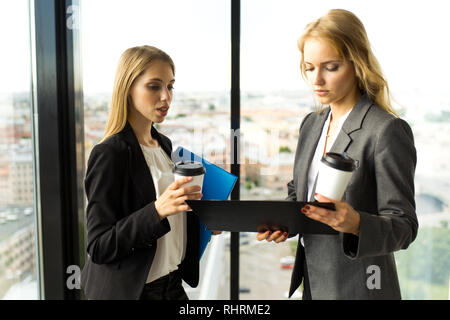 Business Frauen Dokumente und trinken Kaffee im Büro vor dem Panoramafenster mit Blick auf die Stadt Stockfoto