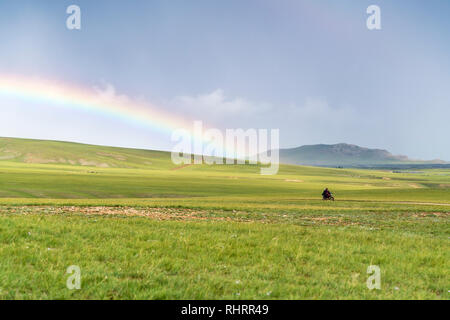 Mann, sein Motorrad und Regenbogen über dem grünen Mongolische Steppe. Ovorkhangai Provinz der Mongolei. Stockfoto