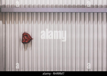 Red beschädigtes Herz geformten Ballon hängend auf einer industriellen Decken Stockfoto