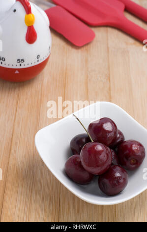 Schöne und leckere rote Kirschen mit einem Hahn Timer auf Holz Hintergrund Stockfoto