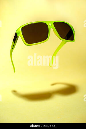 Helle grüne Farbe Sonnenbrille in der Luft. Grüne, die in der Luft schweben Sonnenbrille auf gelben Hintergrund. Untere Schatten unterhalb der Gläser. Minimalismus summ Stockfoto
