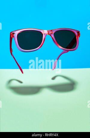 Hell rosa Sonnenbrille in der Luft. In der Luft schweben rosa Sonnenbrille auf Pastelltöne blau und grün hinterlegt. Untere Schatten unter dem Glas Stockfoto