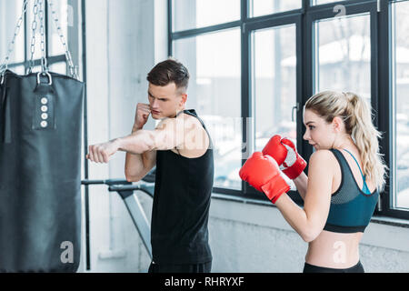 Muskulöse männlichen Trainer und junge Frau in Boxhandschuhe Training mit Boxsack in der Turnhalle Stockfoto