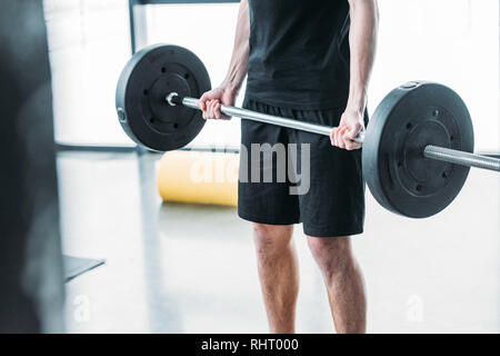 7/8 Schuß des jungen Mannes in Sportkleidung anheben Barbell in der Turnhalle Stockfoto