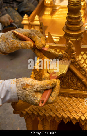 Kambodscha, Phnom Penh, Street 305, behandschuhten Händen der Arbeiter Malerei neue Geist Haus mit Gold Farbe Stockfoto