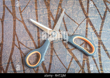 Ansicht von oben in schwarz und orange gefärbt Schere auf eine strukturierte braun Tabelle gehalten Stockfoto