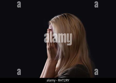 Blonde Frau, die ihr Gesicht mit Handflächen, Weinen, Profil Foto mit dunklen Hintergrund Stockfoto
