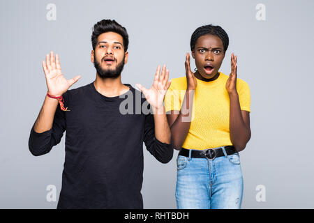 Überrascht neugierige junge interracial Paare, die in derselben Kleidung und Brillen die geballten Fäuste auf ihre Gesichter gekleidet, schreien, öffnen den Mund Stockfoto