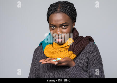 Lächelnd afrikanische Frau im grauen pullover, Schal halten Medikamente Aspirin Tabletten, Pillen auf grauem Hintergrund. Stockfoto