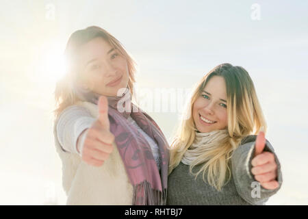 Zwei Freundinnen lächelnd und mit Daumen hoch im Sonnenlicht. Stockfoto