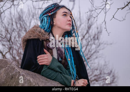 Nachdenkliches Mädchen mit blauen Haaren Dreadlocks in den Wäldern auf den Felsen. Frau viking Träume und in die Ferne schaut Stockfoto