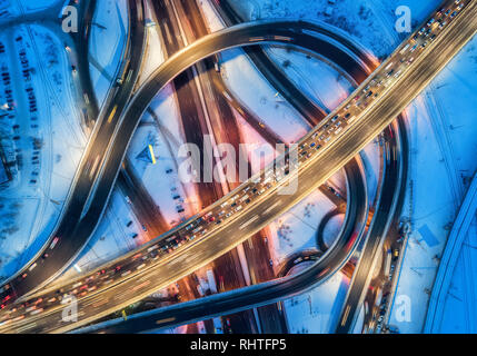 Luftaufnahme der Weg in die moderne Stadt in der Nacht im Winter. Blick von oben auf den Verkehr in Autobahn mit Stadt Ausleuchtung. Autos auf erhöhte Straße und Interchang Stockfoto