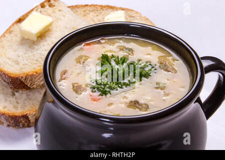 Clam Chowder in einem schwarzen Schüssel mit Petersilie, Brot und Butter auf einem weißen Hintergrund. Stockfoto