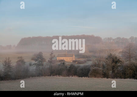 St. Oswalds Kirche im Winter Nebel und Frost bei Sonnenaufgang. Widford, Cotswolds, Oxfordshire, England Stockfoto