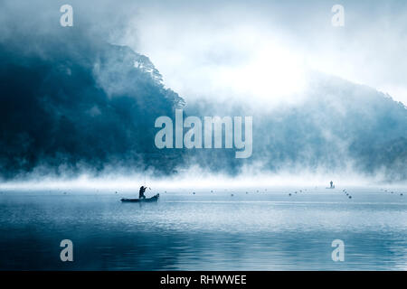 Boot mit Fischer auf See Shōji im Morgennebel. Er erwischt einen Fisch mit seinen Haken. Stockfoto