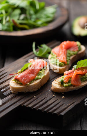 Mini toast Bruschetta mit Lachs und Avocado auf Holz serviert. Selektiver Fokus Stockfoto
